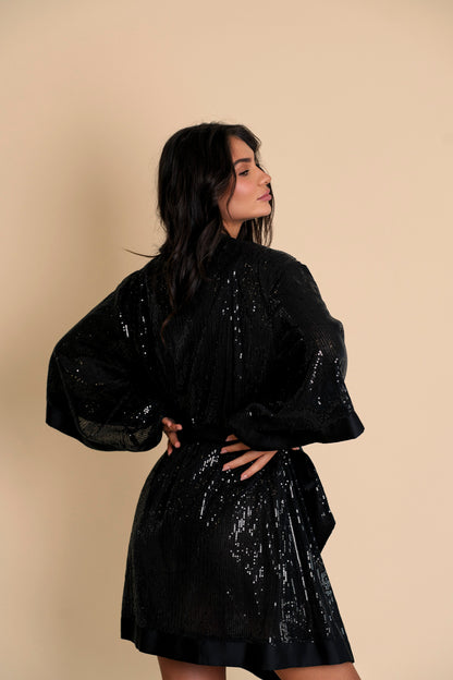 A woman modeling a black Stella Sequin Kimono Robe with sequin fabric and floral neckline detail, paired with a black bodysuit.